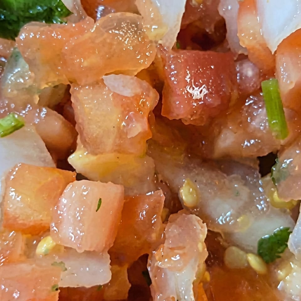 Close-up of diced raw salmon and translucent fish mixed with onion, herbs, and dressing.