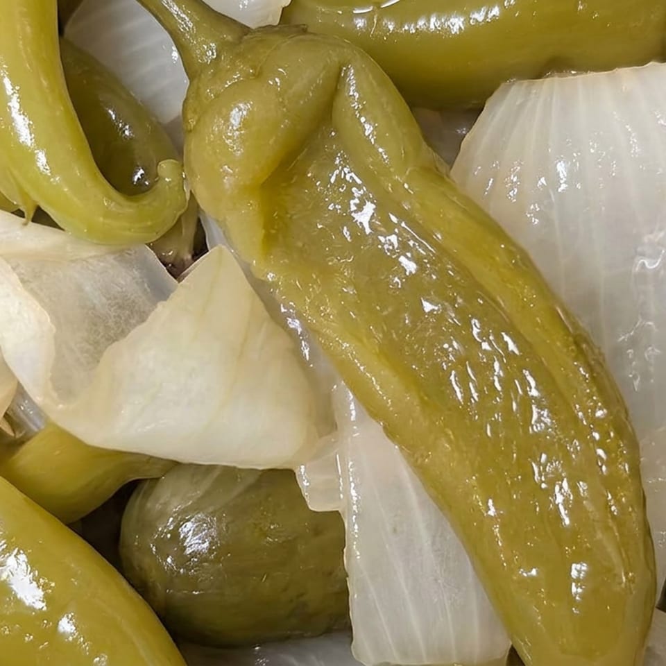 Close-up of glossy pickled green peppers and white onion pieces in a briny mixture.