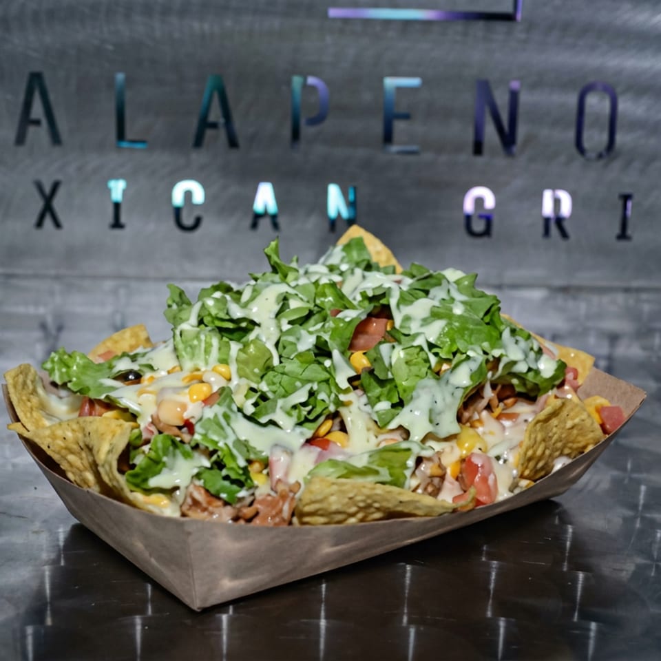 Loaded nachos topped with lettuce, cheese, tomatoes, corn, and creamy sauce in a paper tray at Jalapeños Mexican Grill.